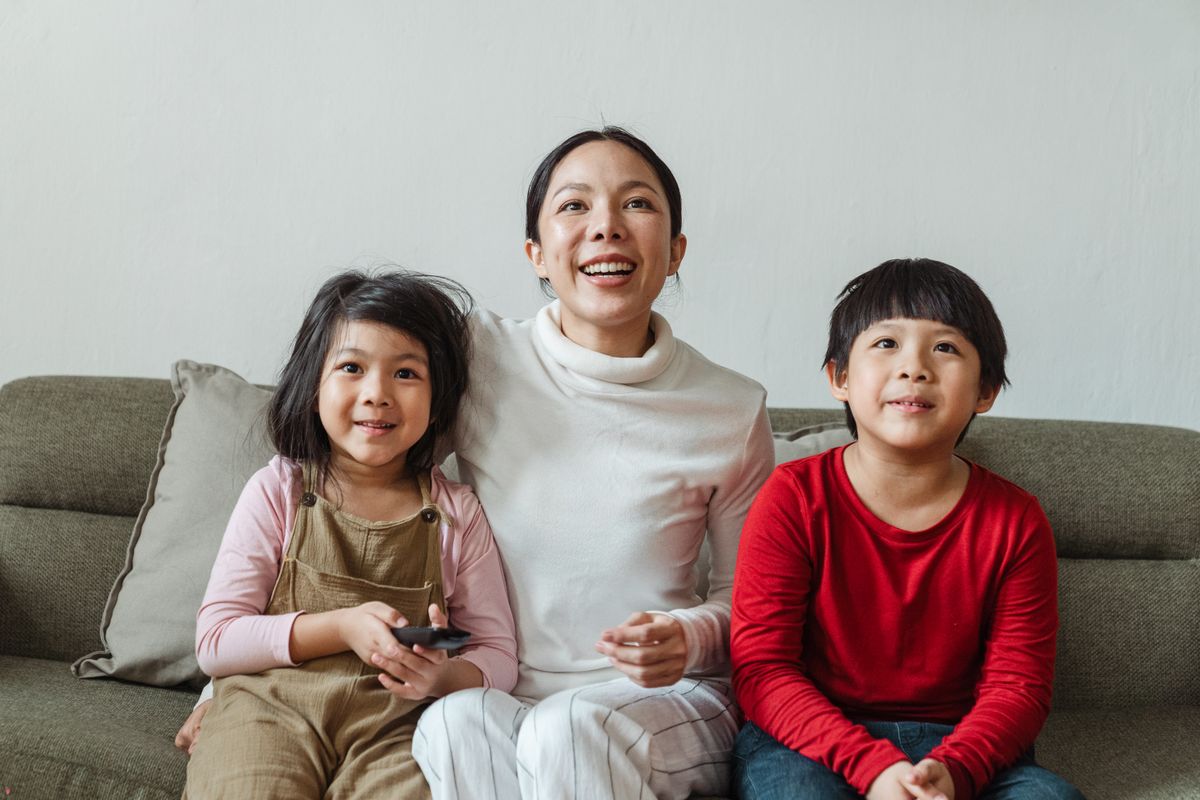 Mãe com filha e filho no sofá assistindo TV